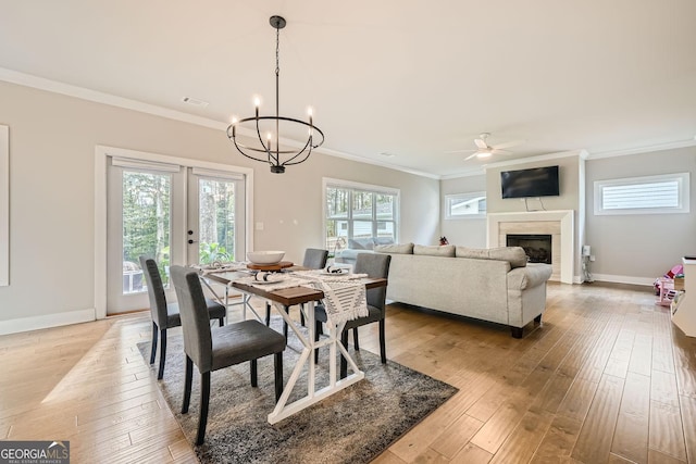 dining area featuring a tile fireplace, french doors, ornamental molding, ceiling fan with notable chandelier, and light wood-type flooring