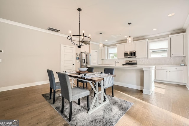 dining space with sink, ornamental molding, light hardwood / wood-style floors, and an inviting chandelier