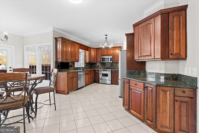 kitchen with ornamental molding, stainless steel appliances, pendant lighting, dark stone countertops, and a chandelier