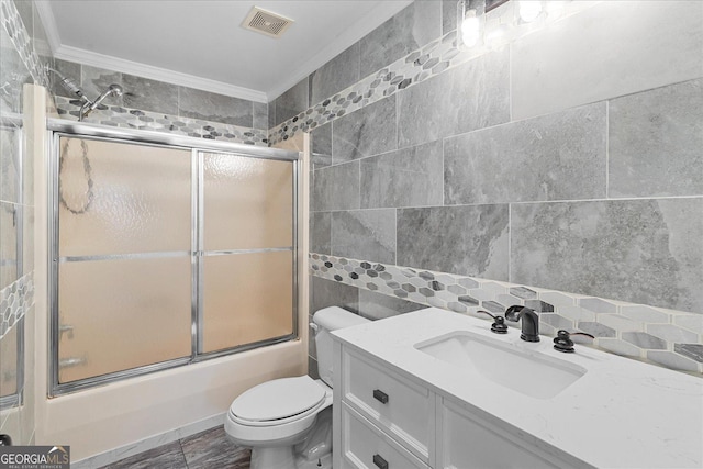 full bathroom with bath / shower combo with glass door, vanity, crown molding, tile walls, and toilet