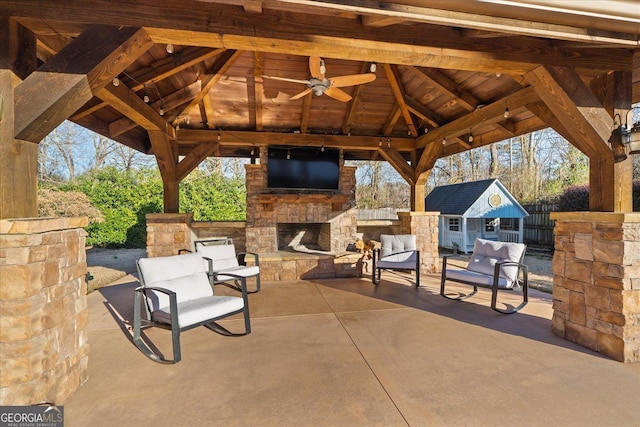 view of patio featuring an outbuilding, a gazebo, an outdoor stone fireplace, and ceiling fan