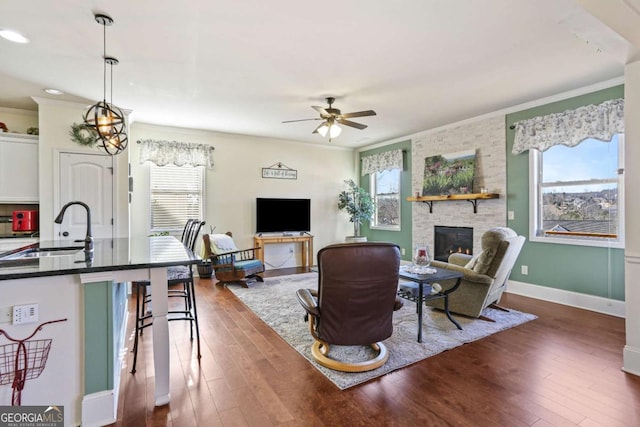 living room with a stone fireplace, a wealth of natural light, sink, and ceiling fan