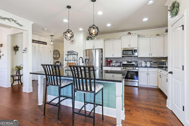 kitchen featuring decorative backsplash, appliances with stainless steel finishes, a kitchen island with sink, white cabinetry, and hanging light fixtures