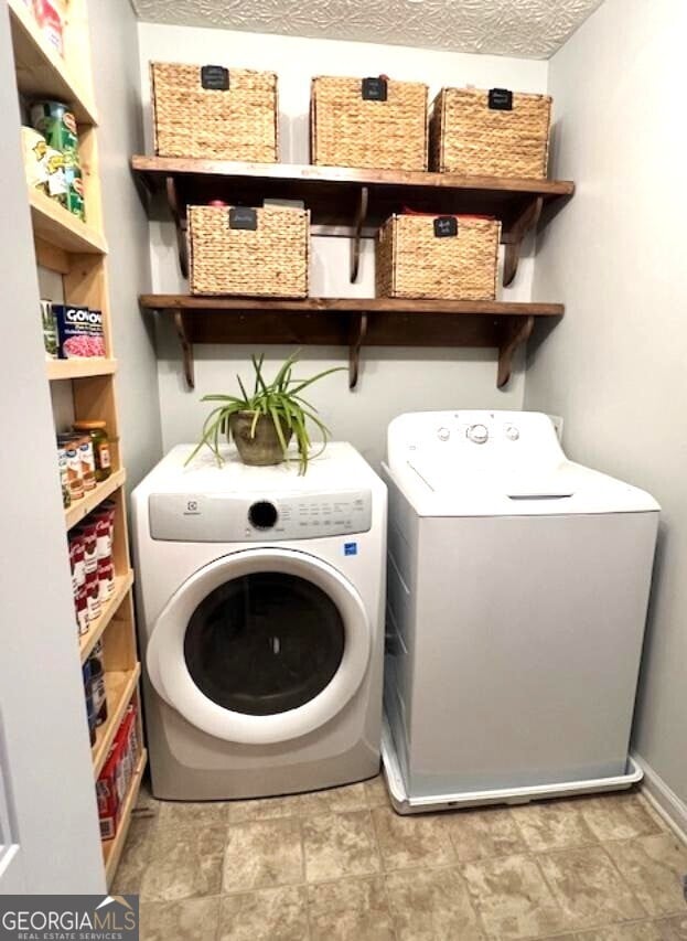 clothes washing area with washing machine and clothes dryer and a textured ceiling