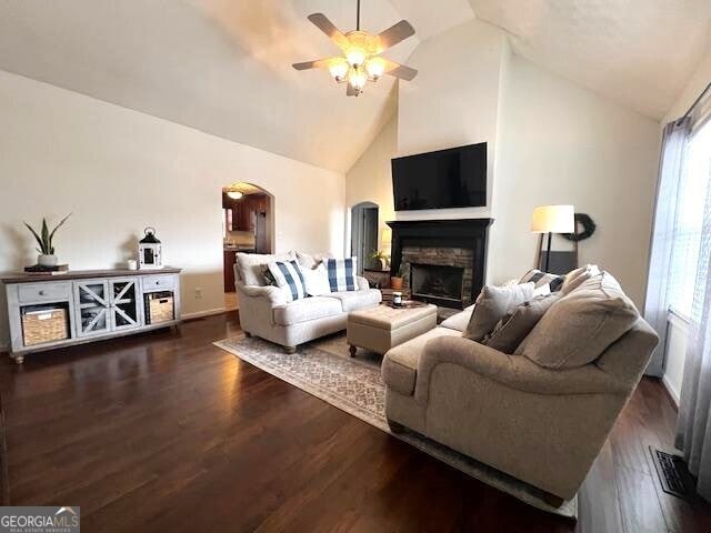 living room with ceiling fan, dark hardwood / wood-style floors, high vaulted ceiling, and a stone fireplace