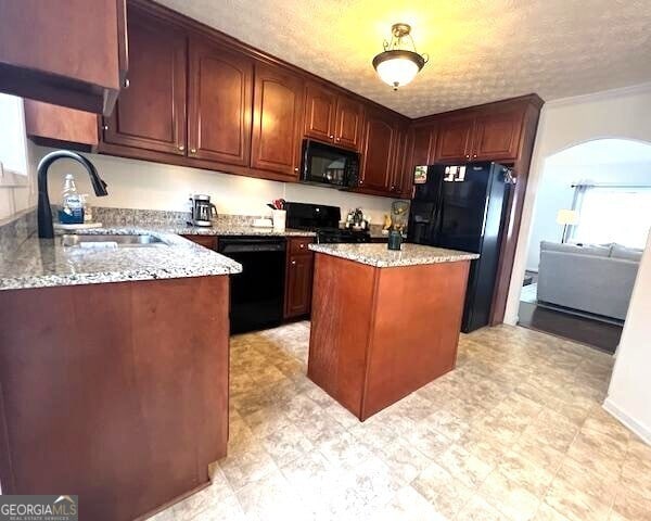 kitchen featuring sink, a center island, a textured ceiling, light stone countertops, and black appliances