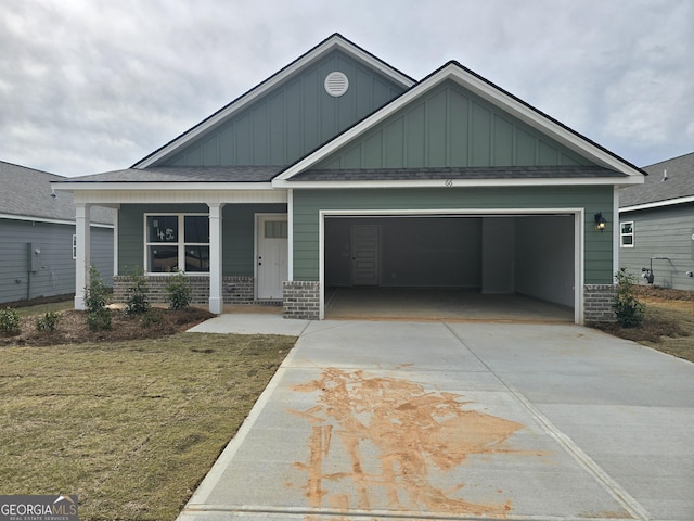 craftsman house featuring an attached garage, covered porch, concrete driveway, a front lawn, and brick siding