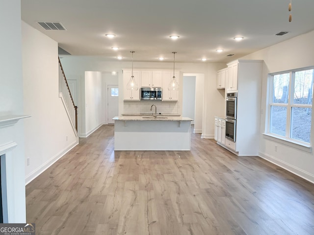 kitchen with hanging light fixtures, appliances with stainless steel finishes, sink, white cabinets, and a kitchen island with sink