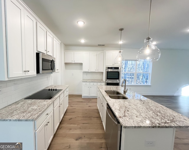 kitchen featuring appliances with stainless steel finishes, white cabinetry, hanging light fixtures, a kitchen island with sink, and sink