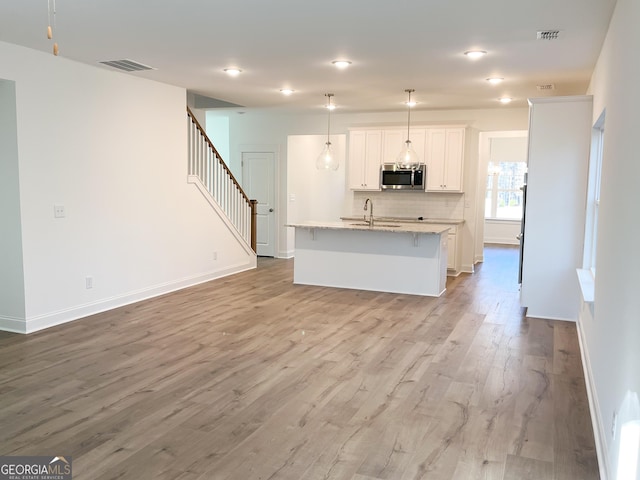 kitchen with a kitchen island with sink, decorative backsplash, white cabinets, decorative light fixtures, and light stone counters