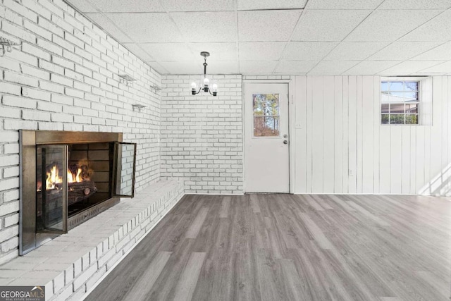 unfurnished living room with a paneled ceiling, a notable chandelier, wood-type flooring, and a fireplace