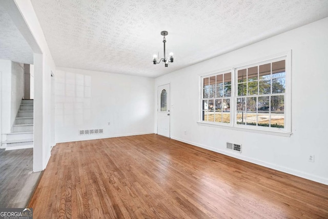 unfurnished living room with a chandelier, wood-type flooring, and a textured ceiling