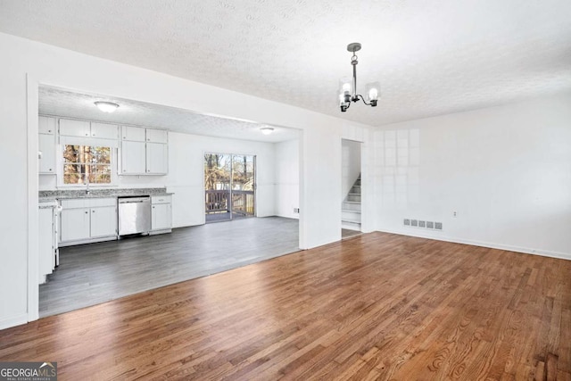 unfurnished living room with a textured ceiling, an inviting chandelier, dark wood-type flooring, and sink