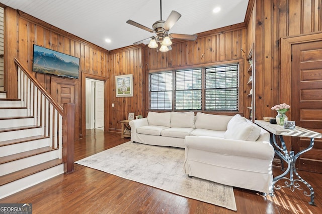 living room featuring dark hardwood / wood-style floors, ceiling fan, crown molding, and wood walls