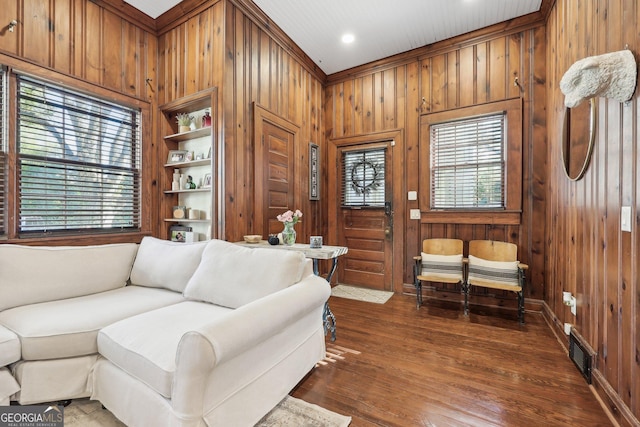 living room with built in shelves, wooden walls, dark hardwood / wood-style flooring, and ornamental molding