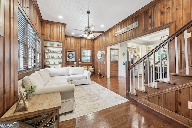 living room with dark hardwood / wood-style flooring, ceiling fan, crown molding, and wood walls