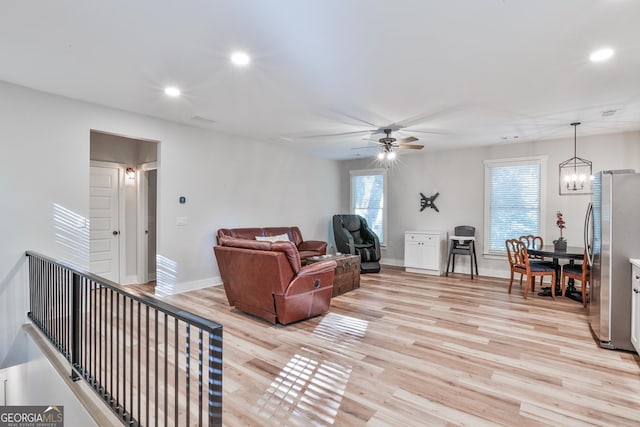 living room featuring ceiling fan with notable chandelier and light hardwood / wood-style flooring