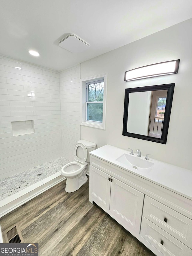 bathroom with tiled shower, hardwood / wood-style flooring, vanity, and toilet