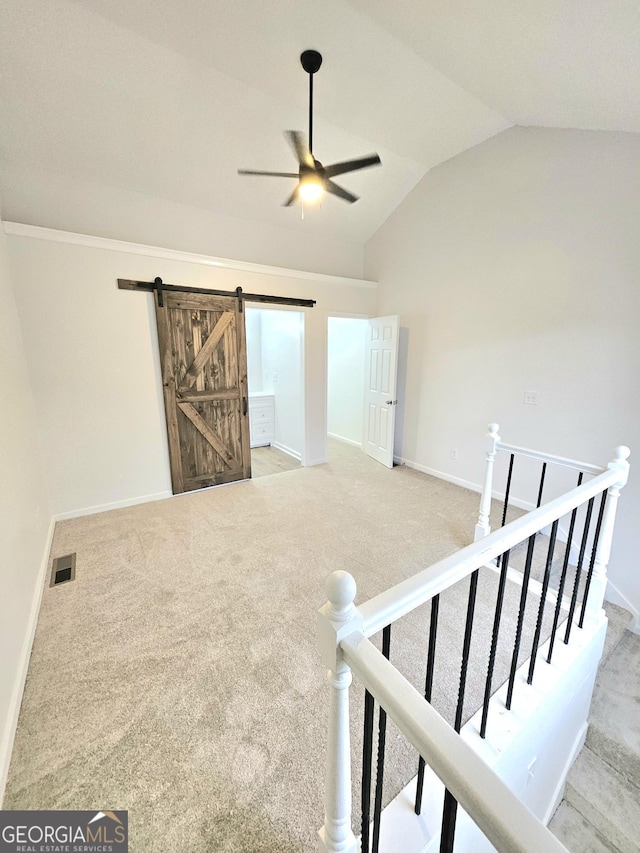 interior space with vaulted ceiling, a barn door, light colored carpet, and ceiling fan