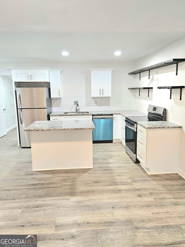 kitchen with appliances with stainless steel finishes, sink, white cabinets, light stone countertops, and light wood-type flooring