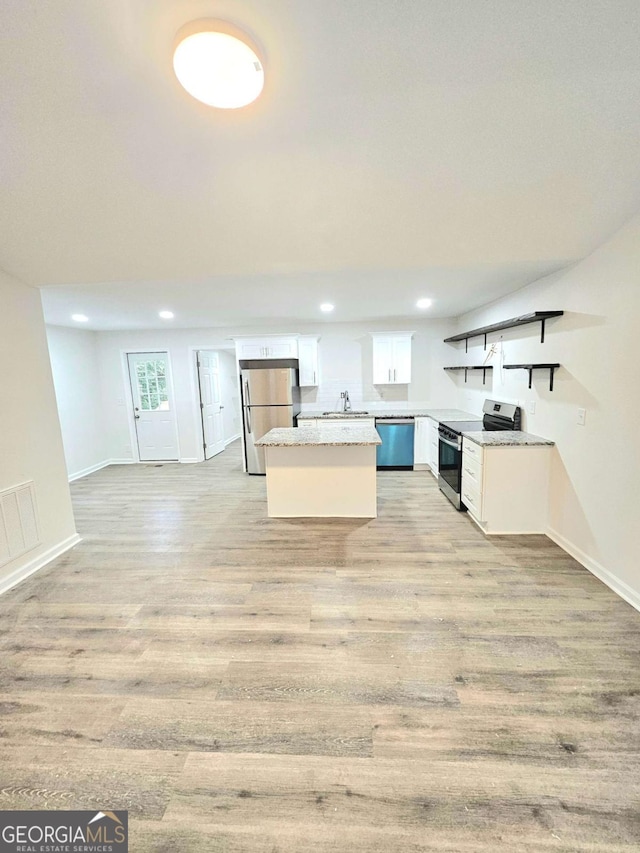 kitchen with appliances with stainless steel finishes, sink, white cabinets, light stone counters, and light hardwood / wood-style floors