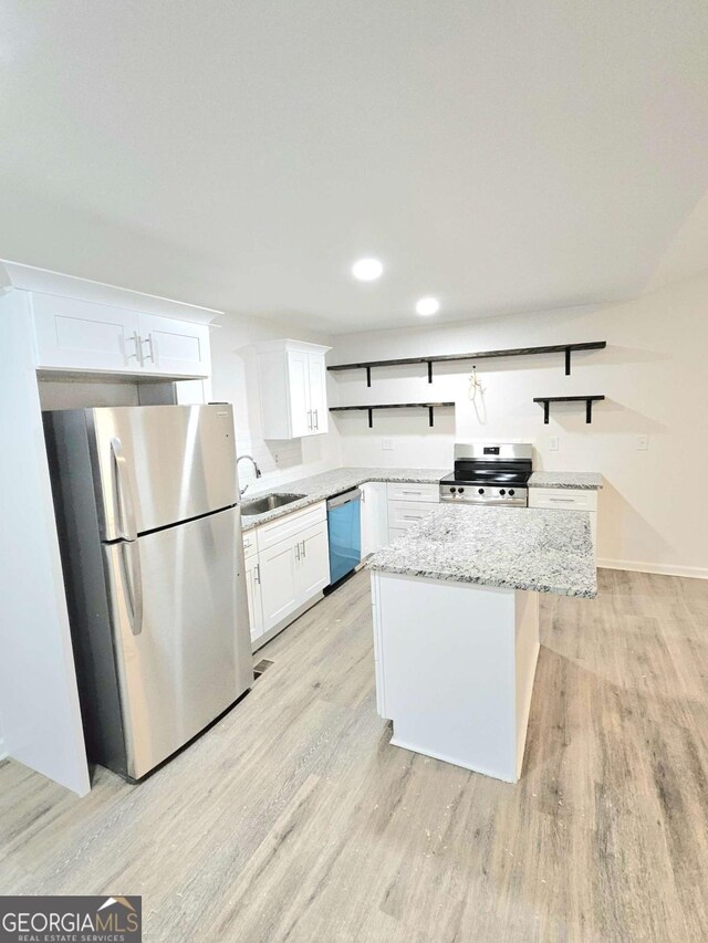 kitchen with white cabinets, sink, a kitchen island, light stone counters, and stainless steel appliances