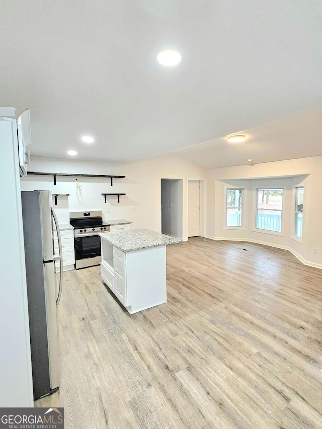 kitchen with appliances with stainless steel finishes, white cabinetry, a center island, light stone counters, and light wood-type flooring