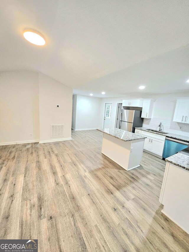 kitchen featuring light stone countertops, appliances with stainless steel finishes, a kitchen island, sink, and white cabinetry