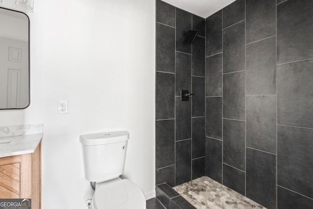 bathroom with tiled shower, vanity, and toilet