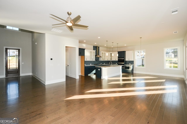 unfurnished living room with ceiling fan with notable chandelier, dark wood-type flooring, and sink