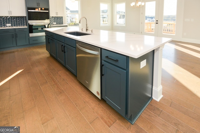 kitchen with dishwasher, sink, a kitchen island with sink, multiple ovens, and decorative backsplash