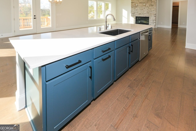 kitchen featuring sink, a stone fireplace, dark hardwood / wood-style flooring, blue cabinets, and a kitchen island with sink