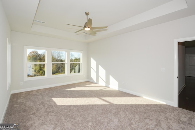 carpeted spare room with a raised ceiling and ceiling fan