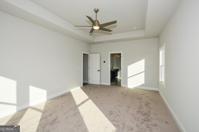 unfurnished bedroom featuring ceiling fan, a spacious closet, light carpet, and a tray ceiling