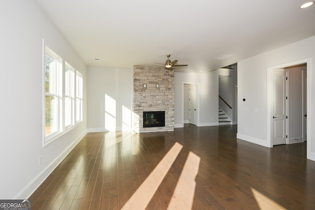 unfurnished living room featuring ceiling fan, a stone fireplace, and dark wood-type flooring