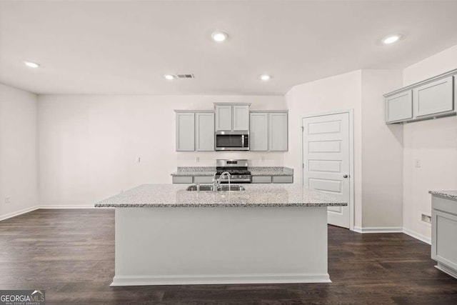 kitchen with gray cabinets, light stone counters, an island with sink, and appliances with stainless steel finishes