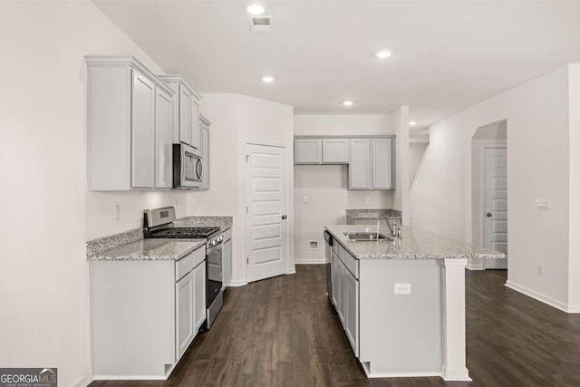 kitchen featuring light stone countertops, sink, stainless steel appliances, dark hardwood / wood-style flooring, and a kitchen island with sink