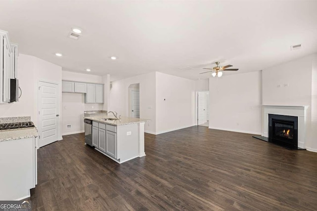 kitchen featuring sink, stainless steel dishwasher, ceiling fan, an island with sink, and light stone counters