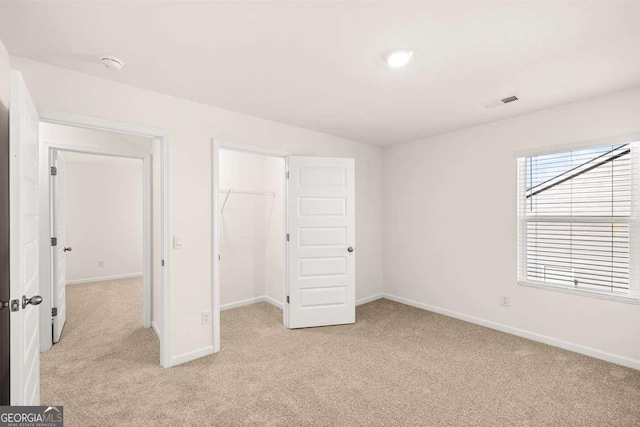 unfurnished bedroom with light carpet, a walk in closet, and a closet