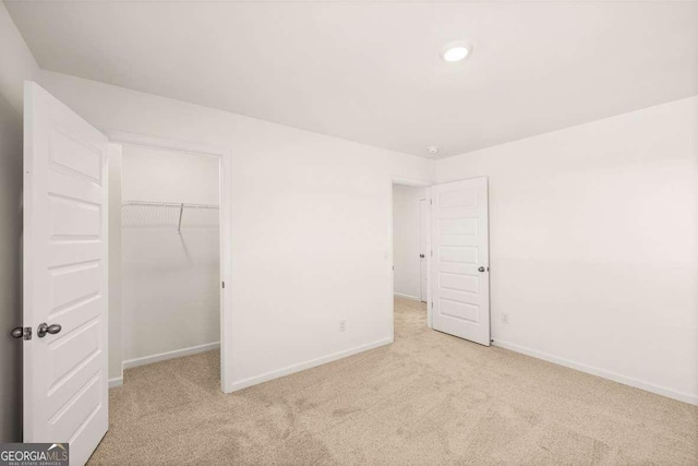 unfurnished bedroom with light colored carpet, a walk in closet, and a closet