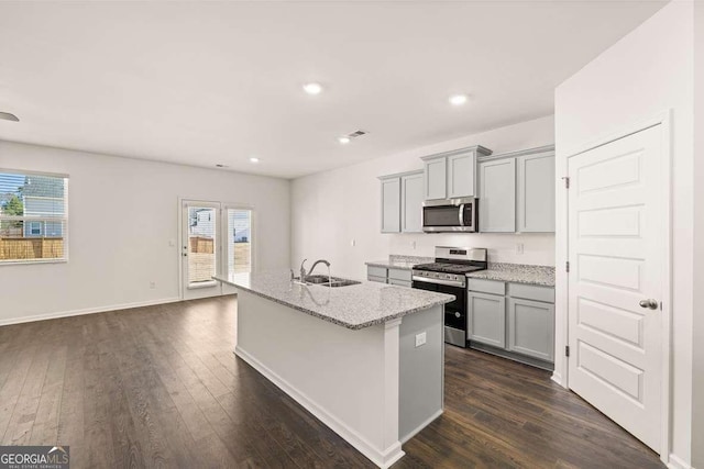 kitchen featuring appliances with stainless steel finishes, light stone counters, gray cabinetry, sink, and a center island with sink