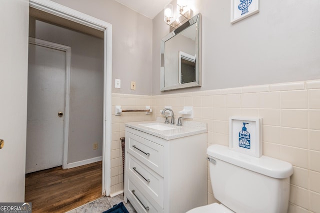 bathroom featuring wood-type flooring, vanity, toilet, and tile walls