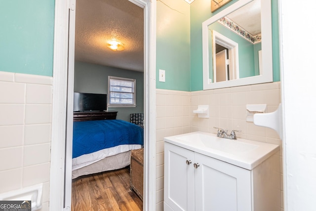 bathroom with hardwood / wood-style flooring, vanity, a textured ceiling, and tile walls