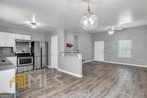 kitchen with stainless steel fridge, stove, tasteful backsplash, white cabinets, and hanging light fixtures