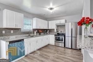 kitchen featuring light stone countertops, white cabinetry, sink, stainless steel appliances, and tasteful backsplash