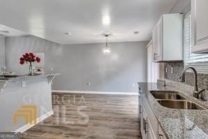 kitchen featuring hardwood / wood-style floors, sink, decorative light fixtures, light stone counters, and white cabinetry