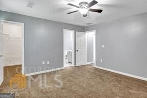 unfurnished bedroom featuring a walk in closet, ceiling fan, a closet, and dark colored carpet