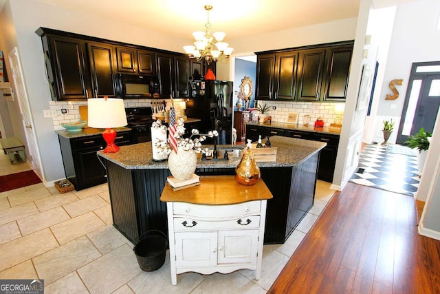 kitchen featuring light stone countertops, a notable chandelier, pendant lighting, a center island with sink, and black appliances