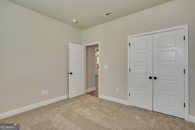 unfurnished bedroom with light colored carpet and a closet