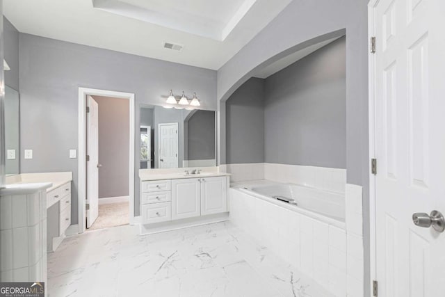 bathroom featuring vanity, tiled bath, and a raised ceiling